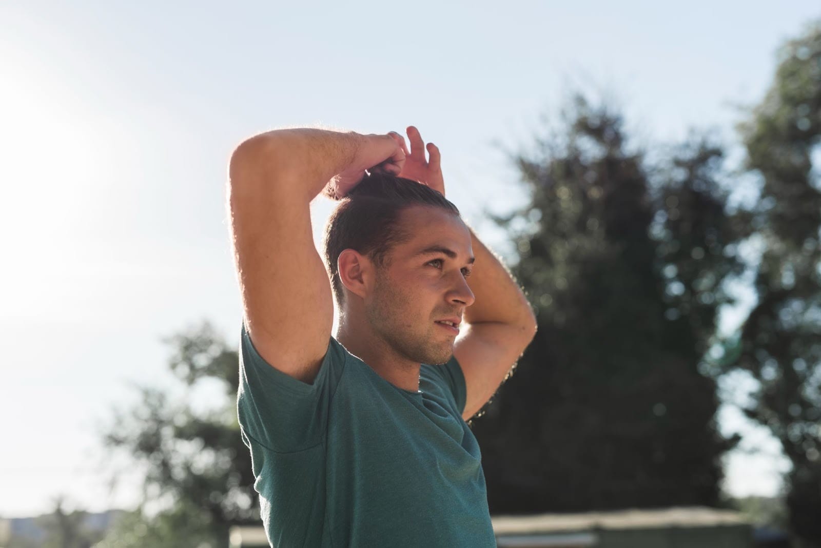 A young man stands outdoors with his hands raised behind his head,with trees and sunlight in the background, reflecting a renewed sense of well-being after HIOP