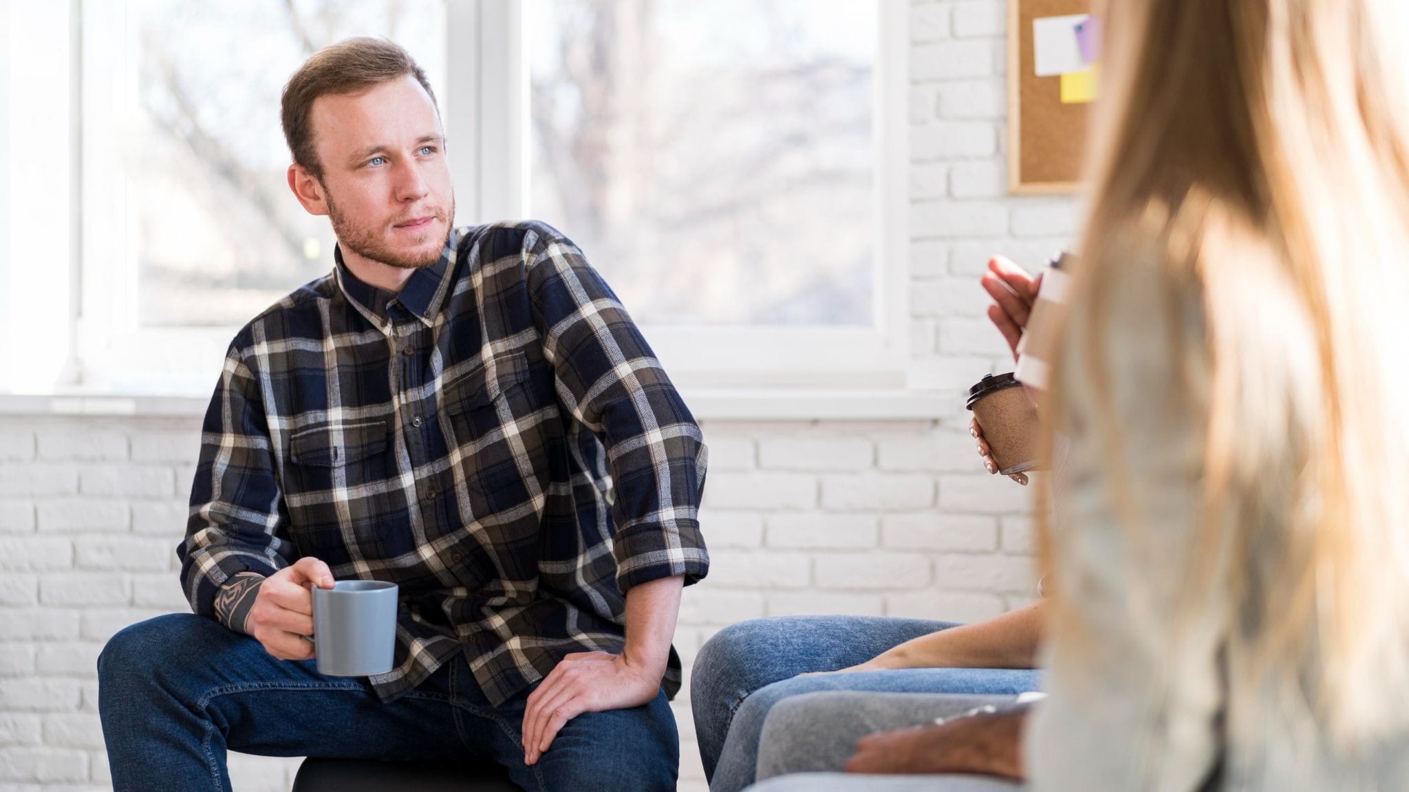 Person in a small group therapy setting holding a mug and listening during a recovery support session