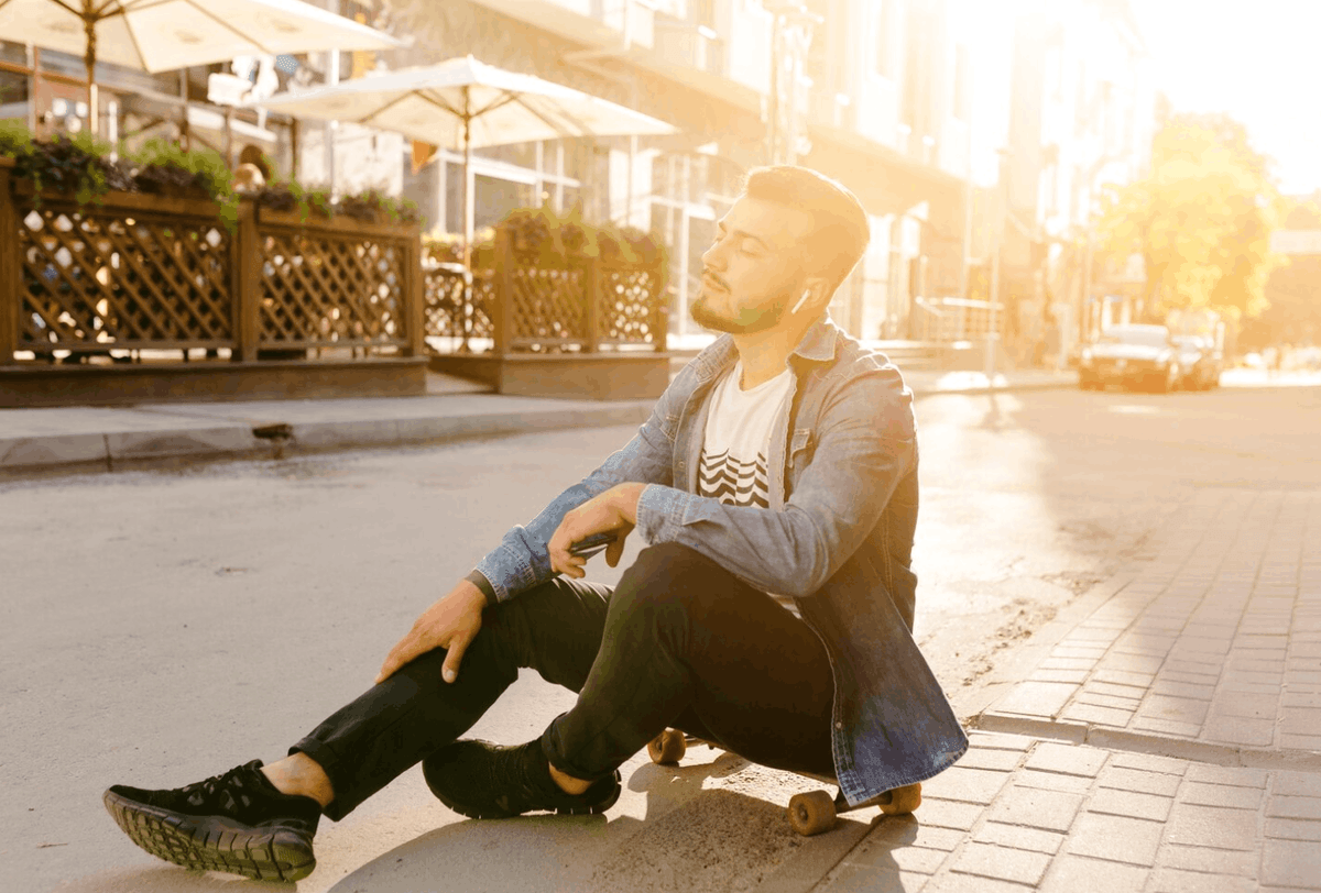 A man sitting alone outdoors while reflecting, representing the challenges of adjusting to everyday life after treatment