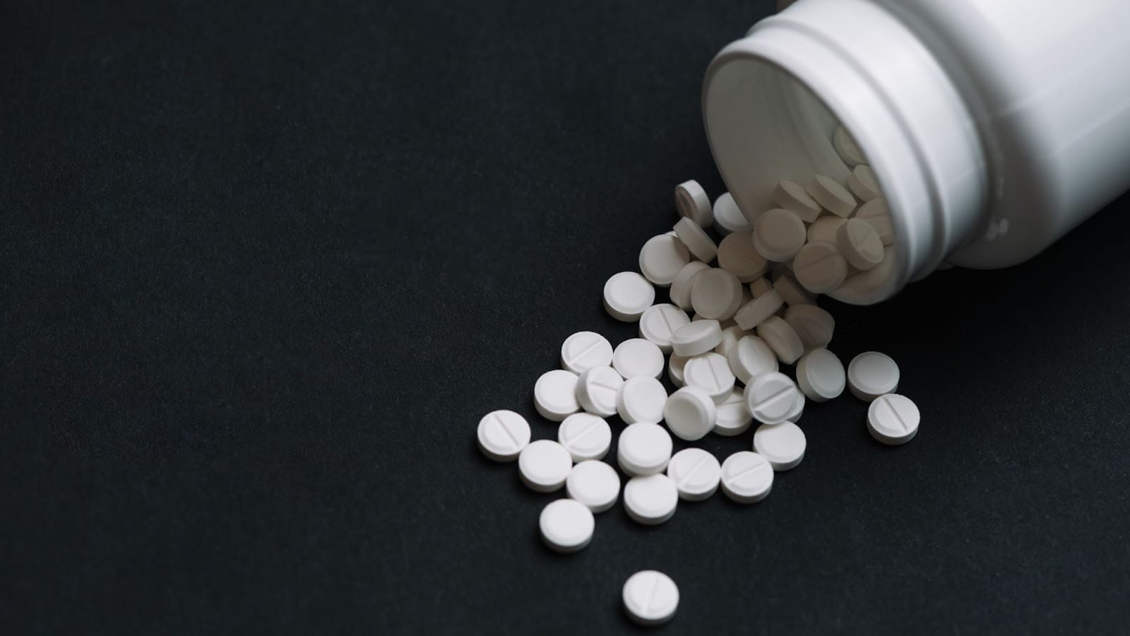 White pills spilled from a bottle, representing the risks and dangers of opioid misuse